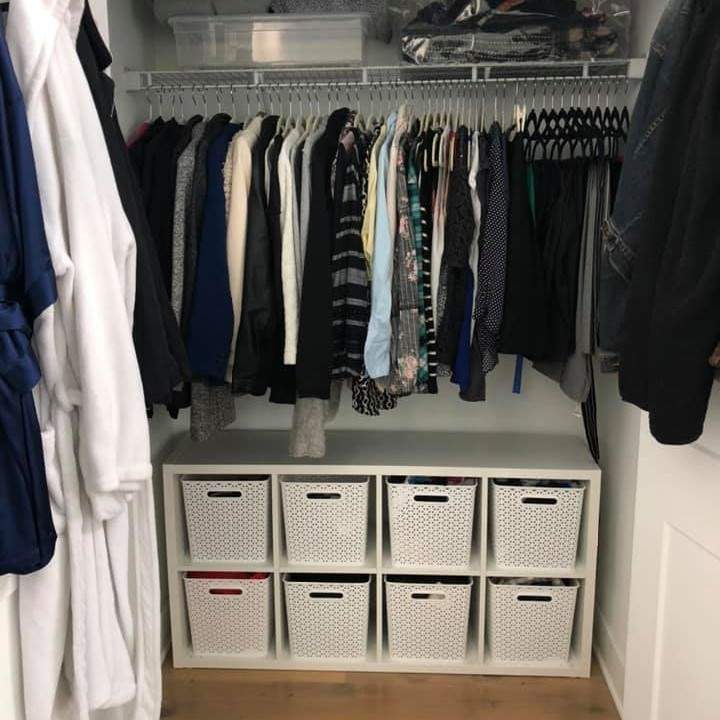 Bedroom closet with professional organizing results. Tops and pants hang on rods. White square bins on the floor contain other clothing categories