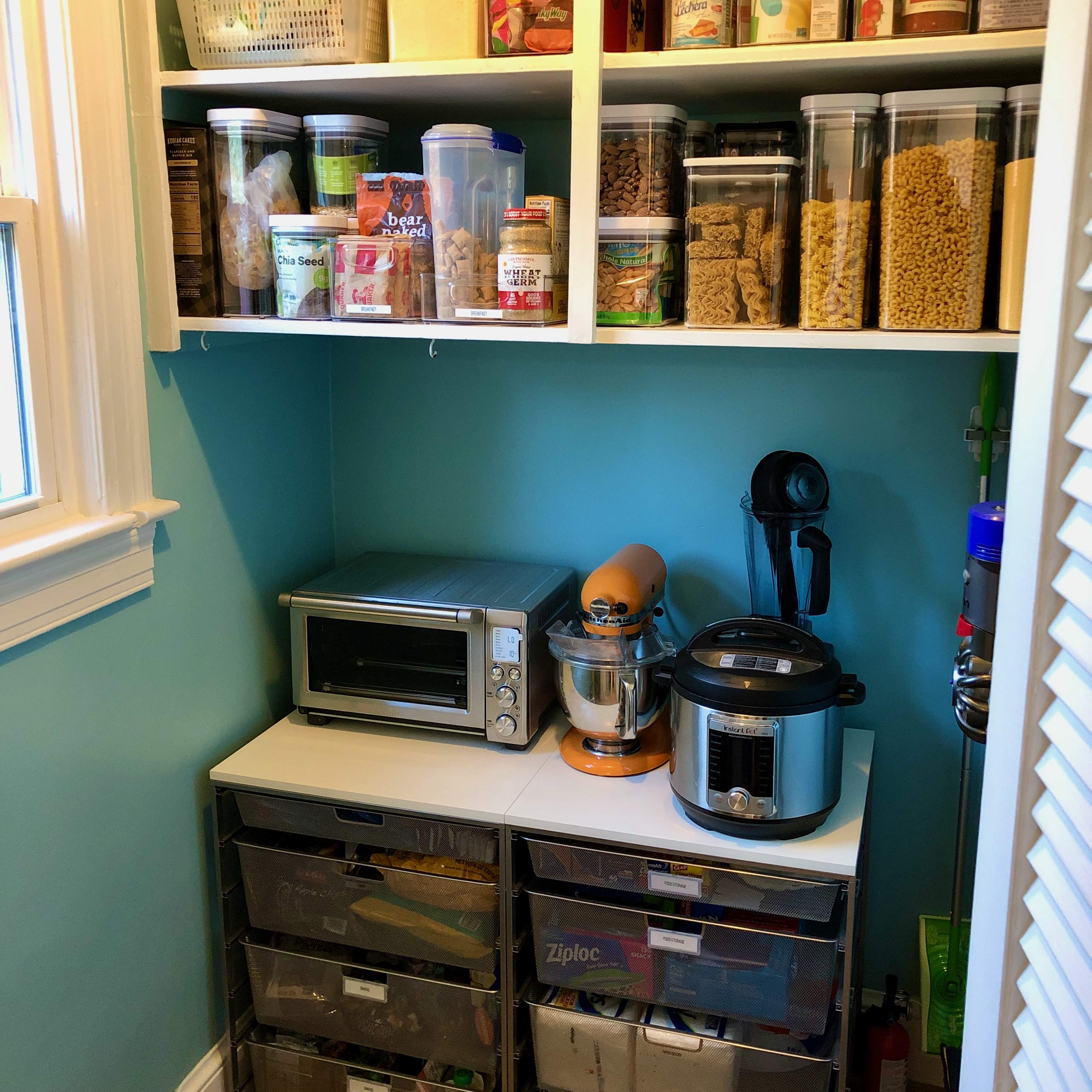 Organized kitchen pantry with Elfa shelving system to hold small appliances; food categories organized on shelves above