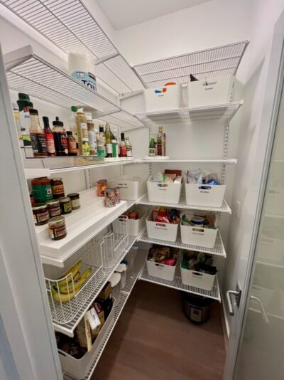 A pantry closet designed with the Elfa system from The Container Store. White shelves were installed, and food items are organized into white bins.